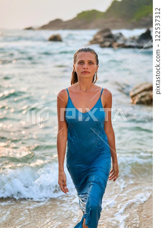 Woman in wet dress exits ocean bay on exotic island beach. Luxury fashion model captivates with beauty and elegance. Inspiration for beauty, skincare, fragrance brands emphasizing tropical allure. Woman in wet dress exits ocean bay on exotic island beach. Luxury fashion model captivates with beauty and elegance. Inspiration for beauty, skincare, fragrance brands emphasizing tropical allure. 122537312
