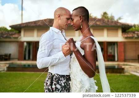Ambiguous gender fluid person in bridal dress, lgbtq groom in bold suit dance at wedding. Tropical villa with rich garden. Celebrates love, diversity, equality at ceremony. Wedding planners use theme. 122537339