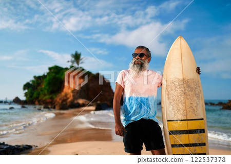 Elderly man with surfboard on sunny beach. Active senior enjoying ocean view, healthy retirement lifestyle adventure. Surfing as leisure in golden years. Celebrating vitality, new experiences. Elderly man with surfboard on sunny beach. Active senior enjoying ocean view, healthy retirement lifestyle adventure. Surfing as leisure in golden years. Celebrating vitality, new experiences. 122537378