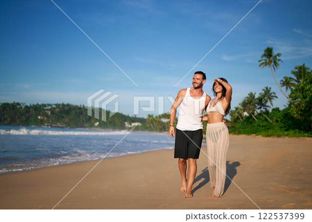 Happy couple strolls on sandy beach at tropical destination. Romantic walk, shoreline embrace, leisure in paradise. Newlyweds enjoy honeymoon, coastal scenery, summer love. Peaceful vacation moment. Happy couple strolls on sandy beach at tropical destination. Romantic walk, shoreline embrace, leisure in paradise. Newlyweds enjoy honeymoon, coastal scenery, summer love. Peaceful vacation moment. 122537399