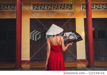 back of a Vietnamese tourist woman in Non La hat with fan at a pagoda temple in Vietnam on trip to Asia 122538118