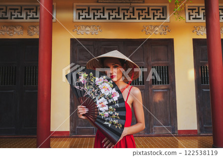 beautiful young woman tourist with a fan in a Vietnamese traditional non la hat at pagoda on a trip in Nha Trang in Vietnam in Asia 122538119