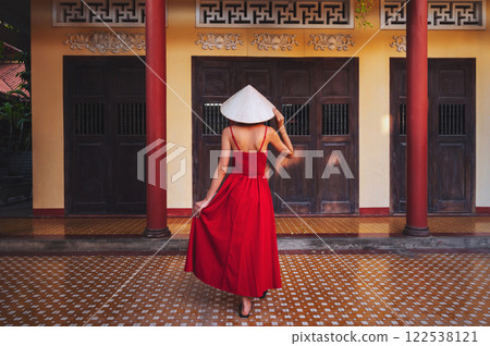 back of a beautiful woman traveler in a dress and a traditional Vietnamese hat at pagoda in Vietnam on a travel to Asia 122538121
