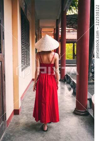 back of a beautiful woman traveler in a dress and a traditional Vietnamese hat at pagoda in Vietnam on a travel to Asia 122538122