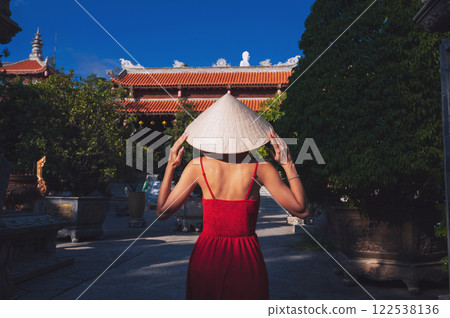 back of beautiful female traveler in a dress and a traditional Vietnamese hat Non La at a pagoda in Vietnam on a travel to Asia 122538136