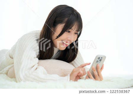 A Japanese woman lying face down and looking at her smartphone 122538367