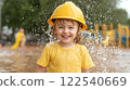 cheerful child wearing yellow helmet and shirt enjoys playing in water splashes outdoors 122540669