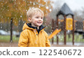 cheerful child in yellow raincoat enjoying rainy day at playground with autumn leaves in background 122540672
