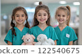Three smiling girls in veterinarian scrubs holding stuffed animals, showcasing care and compassion 122540675