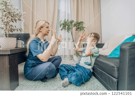 female therapist and boy practicing hand gestures in therapy session, cozy home setting, concept of child development and alternative communication female therapist and boy practicing hand gestures in therapy session, cozy home setting, concept of child development and alternative communication 122541101