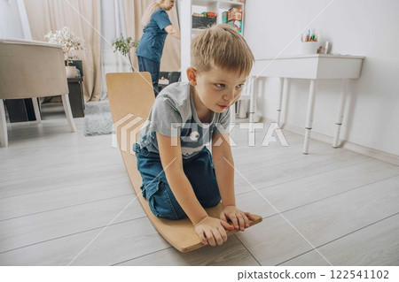 boy on wooden balance board in with therapist in background organizing materials concept of therapy, child development, motor skills training boy on wooden balance board in with therapist in background organizing materials concept of therapy, child development, motor skills training 122541102