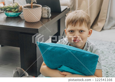 angry boy hugs a bright blue pillow in a cozy home environment, looks at the camera - the concept of children's emotions, humor and relaxation indoors. angry boy hugs a bright blue pillow in a cozy home environment, looks at the camera - the concept of children's emotions, humor and relaxation indoors. 122541108