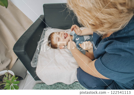 boy lying on soft white blanket during speech therapy session with female therapist in cozy room, concept of speech correction, childhood development, and healthcare 122541113