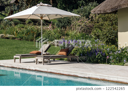 white sunshade casts a shadow over two cushioned lounge chairs 122542265