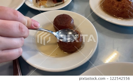 Close-up of Two Gulab Jamun Resting in a Light Syrup on a Small, White Ceramic Plate 122542556