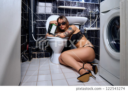 Drunk young woman lying hugging a toilet in a restroom 122543274