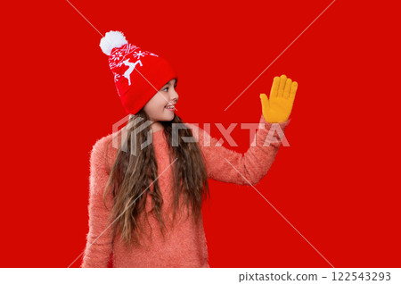 Girl enjoying winter style. Teen girl wearing stylish new year hat. Childhood winter memories. Teen girl kid isolated on red studio. Child winter fashion. Teenage style 122543293