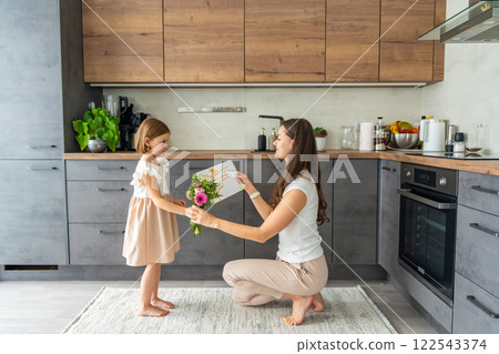 Little girl giving bouquet of flowers and drawing to her mum on the home kitchen. Mothers day, birthday or International Women's Day 8 march concept 122543374