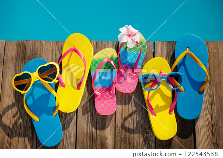 Beach flip-flops and sunglasses on wooden planks near swimming pool 122543538