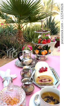 Creamy cake roll placed next to cup on wooden table, ornate silver tray adding rustic elegance. Cup and cake together enhance outdoor dessert ambiance. Wooden display concept. Creamy cake roll placed next to cup on wooden table, ornate silver tray adding rustic elegance. Cup and cake together enhance outdoor dessert ambiance. Wooden display concept. 122543626