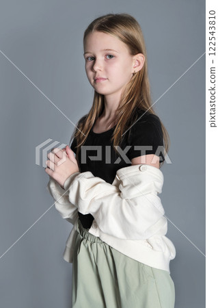 A young girl in a black top and green pants stands with her hands together, looking away with a pensive expression. This image highlights the contemplative nature of children, capturing a serene and A young girl in a black top and green pants stands with her hands together, looking away with a pensive expression. This image highlights the contemplative nature of children, capturing a serene and 122543810