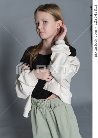 A young girl in a black shirt and light green pants stands thoughtfully, her hands gently clasped. This image reflects the calm and introspective side of childhood, emphasizing the depth of young A young girl in a black shirt and light green pants stands thoughtfully, her hands gently clasped. This image reflects the calm and introspective side of childhood, emphasizing the depth of young 122543812