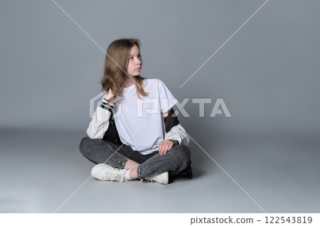 A girl in a casual outfit sits cross-legged, lost in thought. This image highlights the blend of innocence and emerging maturity, symbolizing the journey of self-discovery and individuality. A girl in a casual outfit sits cross-legged, lost in thought. This image highlights the blend of innocence and emerging maturity, symbolizing the journey of self-discovery and individuality. 122543819