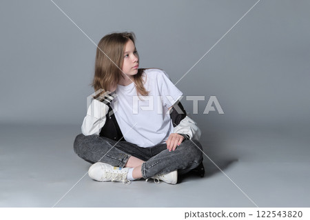 A young girl sits cross-legged on the floor, gazing thoughtfully to the side. This image captures a serene moment, reflecting the introspective nature and calm confidence of youth. 122543820