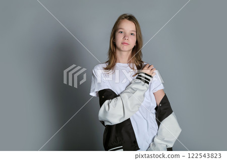 A young girl casually holds her jacket and looks down thoughtfully. This image reflects a moment of introspection, capturing the complexity of youth and the search for self-identity. A young girl casually holds her jacket and looks down thoughtfully. This image reflects a moment of introspection, capturing the complexity of youth and the search for self-identity. 122543823