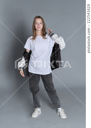 The young girl holds her jacket in a laid-back manner, eyes cast down. This portrait represents the quiet moments of reflection that often accompany growing up and self-expression. 122543829
