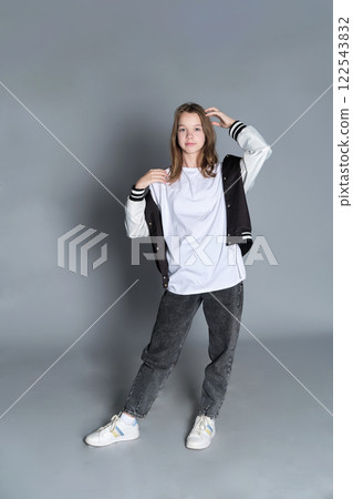 A young girl stands confidently in casual attire, one hand resting on her jacket. This image showcases the modern approach to youth fashion, blending comfort with a sense of style. A young girl stands confidently in casual attire, one hand resting on her jacket. This image showcases the modern approach to youth fashion, blending comfort with a sense of style. 122543832