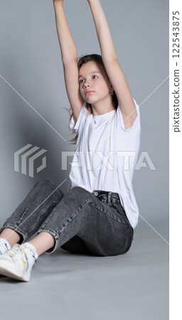 A girl sits comfortably on the floor, leaning forward slightly with her hands on her sneakers. This portrait reflects the trend of minimalistic and natural photography that showcases authenticity. A girl sits comfortably on the floor, leaning forward slightly with her hands on her sneakers. This portrait reflects the trend of minimalistic and natural photography that showcases authenticity. 122543875