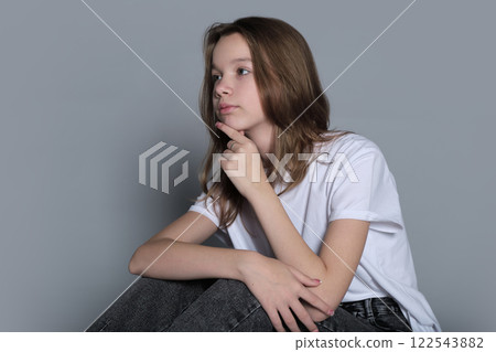 A young girl sits thoughtfully with her hand resting on her chin, wearing casual clothes. This portrait captures the calm introspection and simplicity of modern youth culture. 122543882