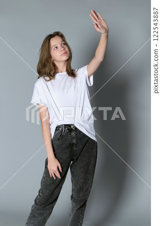 A young girl in a white t-shirt and jeans raises her arm thoughtfully. The image captures a moment of introspection and the youthful desire to reach beyond limitations. A young girl in a white t-shirt and jeans raises her arm thoughtfully. The image captures a moment of introspection and the youthful desire to reach beyond limitations. 122543887