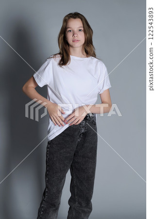A teenage girl stands confidently in a casual outfit, wearing a white t-shirt and jeans. The simple pose and minimalistic setting reflect a natural and modern sense of style. A teenage girl stands confidently in a casual outfit, wearing a white t-shirt and jeans. The simple pose and minimalistic setting reflect a natural and modern sense of style. 122543893