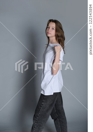 A teenage girl stands confidently, looking over her shoulder while holding her t-shirt. Her casual outfit and strong posture reflect individuality and modern youth empowerment. A teenage girl stands confidently, looking over her shoulder while holding her t-shirt. Her casual outfit and strong posture reflect individuality and modern youth empowerment. 122543894