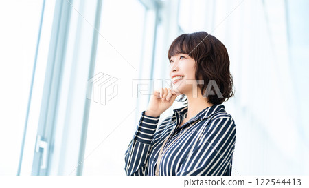 Smiling woman/businesswoman looking out the window Smiling woman/businesswoman looking out the window 122544413