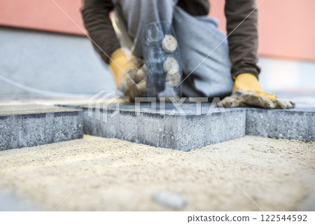 Builder tamping down a new paving slab or brick with motion blure effect 122544592