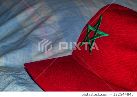 Bright red cap baseball cap with a green five-pointed star symbolizing the national flag of the Kingdom of Morocco in North Africa, a souvenir item from a summer vacation trip Bright red cap baseball cap with a green five-pointed star symbolizing the national flag of the Kingdom of Morocco in North Africa, a souvenir item from a summer vacation trip 122544943
