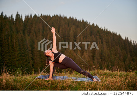 Woman practicing yoga outdoors in the mountains in a serene, natural setting. Female performing yoga pose on mat, with backdrop of beautiful mountain landscape at sunrise or sunset. Woman practicing yoga outdoors in the mountains in a serene, natural setting. Female performing yoga pose on mat, with backdrop of beautiful mountain landscape at sunrise or sunset. 122544973