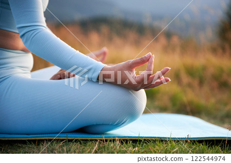 Close up of woman's hands on dawn background in the evening. Woman doing yoga exercise and meditating during sunset in mountains Close up of woman's hands on dawn background in the evening. Woman doing yoga exercise and meditating during sunset in mountains 122544974