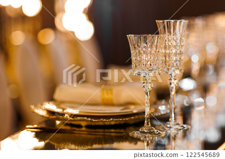 Luxury table setting with plates, napkin with ring, crystal wineglasses and golden cutlery on mirror table for romantic dinner in restaurant, bokeh. Christmas, New Year 2026 dinner. Wedding, birthday 122545689