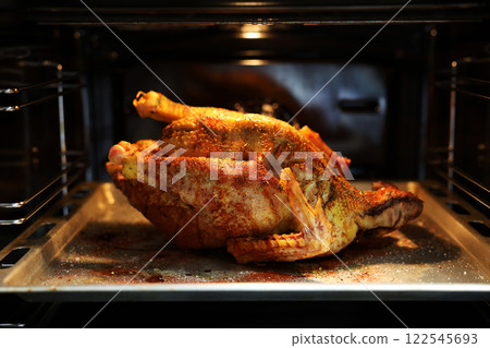 Festive christmas roast whole duck on aluminized steel baking sheet inside open oven at home kitchen. Ready golden turkey or goose on tray. Classic American Thanksgiving food preparation. 122545693