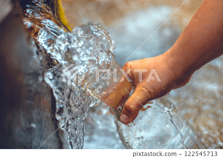 Pure water from the spring is collected in a glass bottle. Transparent cold water from a natural spring pours into a bottle in the autumn forest. Water source concept. 122545713