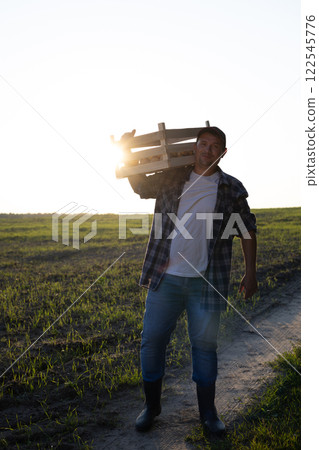 vertically. A farmer with a box of potatoes stands in a field against the backdrop of a beautiful sunset. The concept of agriculture and small business Farmer at the end of the day after the harvest. 122545776