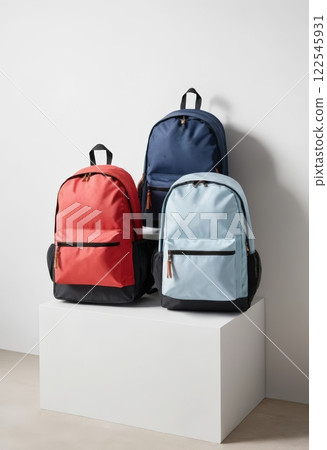 A frontal view of three backpacks in red, navy, and soft blue, displaying modern design and functionality. Ideal for fashion retailers or outdoor gear enthusiasts. A frontal view of three backpacks in red, navy, and soft blue, displaying modern design and functionality. Ideal for fashion retailers or outdoor gear enthusiasts. 122545931