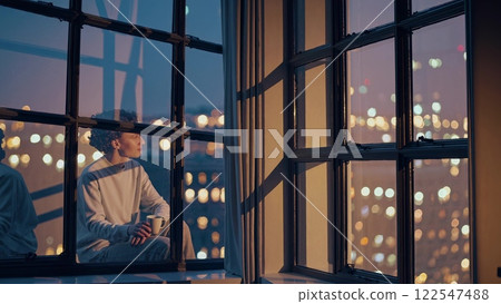 Young man relaxing and enjoying night city view from window 122547488