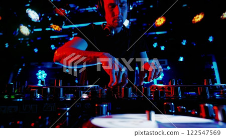 DJ Mixing Music on Turntable in Nightclub with Vibrant Lights DJ Mixing Music on Turntable in Nightclub with Vibrant Lights 122547569