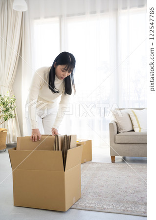A woman breaking down cardboard boxes and tidying up A woman breaking down cardboard boxes and tidying up 122547786