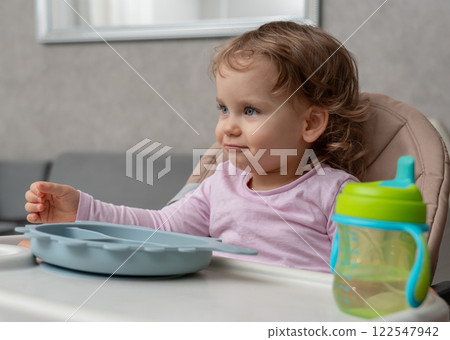 A curious toddler enjoying mealtime with a sippy cup and playful expression. A curious toddler enjoying mealtime with a sippy cup and playful expression. 122547942